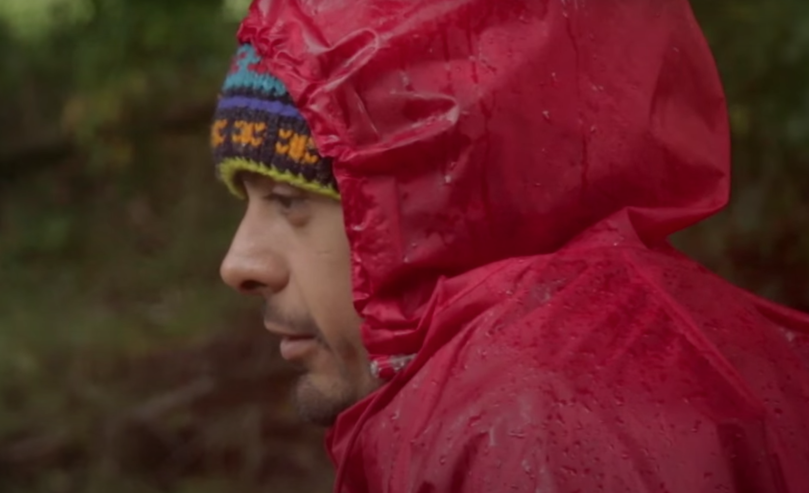 Felipe, con un gorro de lana de colores y una parka roja para la lluvia mira el agua desde un bosque