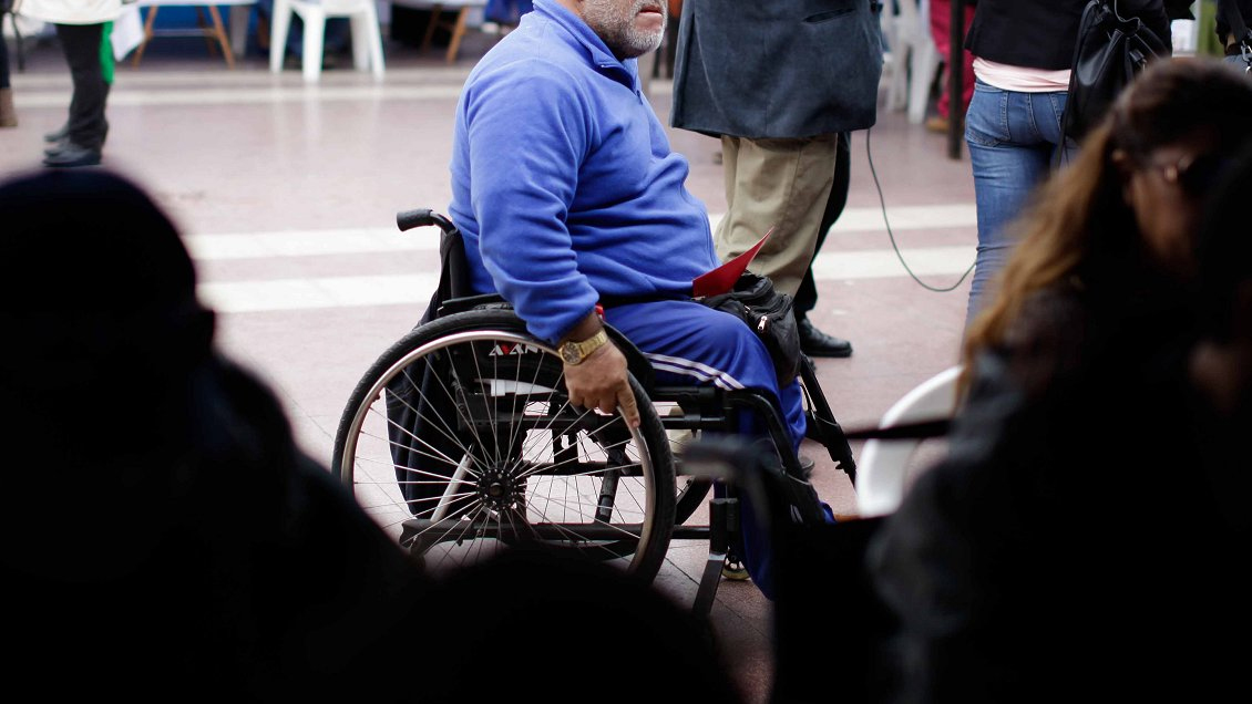 foto de un hombre en silla de ruedas en una fila de votaciones, está vestido de azul